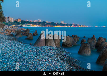 Una lunga esposizione foto del calcestruzzo massi conica giacente in mare sullo sfondo della costa di sochi al crepuscolo, Russia Foto Stock