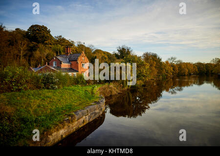 Un paesaggio autunnale con una grande casa di mattoni sulle rive del fiume Tessitore a Northwich, Cheshire. Foto Stock
