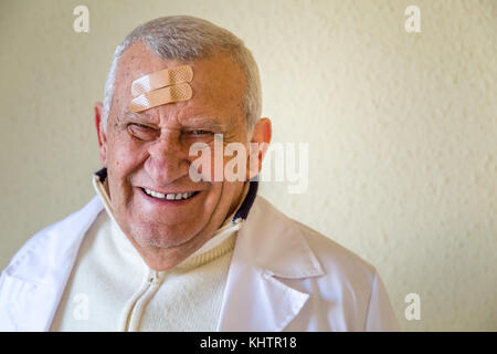 Il vecchio medico con patch sulla fronte sorridente Foto Stock