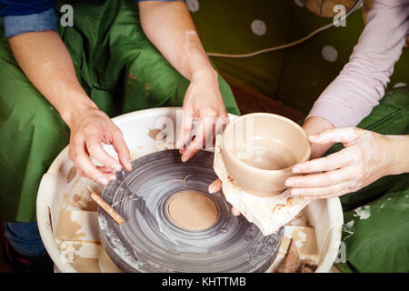 Close-up di una giovane donna potter insegna a scolpire una donna su un tornio del vasaio un vaso fatto di argilla marrone, lo taglia il tornio del vasaio con una specia Foto Stock