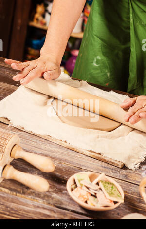 Close-up di una giovane donna potter in un grembiule verde lanciando una gabbia di creta per fare una piastra, su di un tavolo di legno ci sono strumenti e spazzole in ba Foto Stock