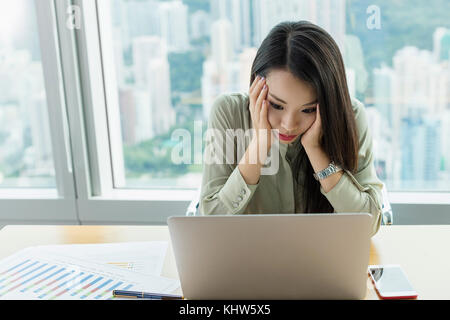 Imprenditrice utilizzando laptop, testa in mani cercando sottolineato Foto Stock