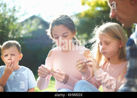 Padre e figli, seduti in giardino, mangiando caramelle Foto Stock