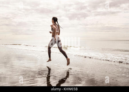 Vista posteriore del giovane femmina runner correre a piedi nudi lungo il bordo d'acqua a beach Foto Stock