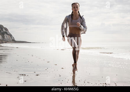 Vista frontale del giovane femmina runner correre a piedi nudi lungo la spiaggia Foto Stock