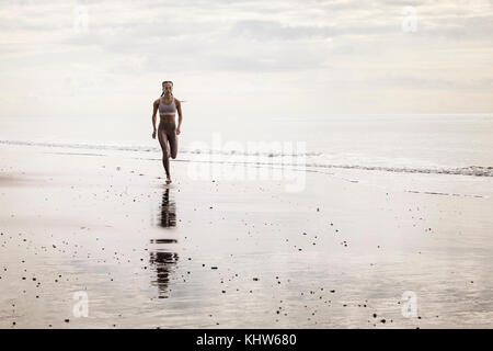 Giovane donna che corre lungo la spiaggia Foto Stock