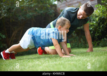 Padre e figlio che esercitano in giardino, facendo push-up Foto Stock