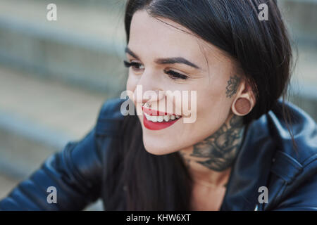 Ritratto di giovane donna sorridente, tatuaggi sul collo, naso e orecchio piercing, close-up Foto Stock