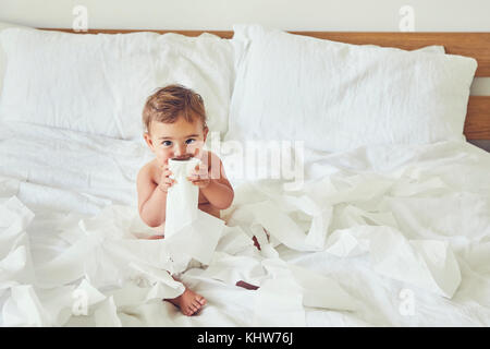 Bambino seduto sul letto, tenendo svelato un nuovo rotolo di carta igienica Foto Stock