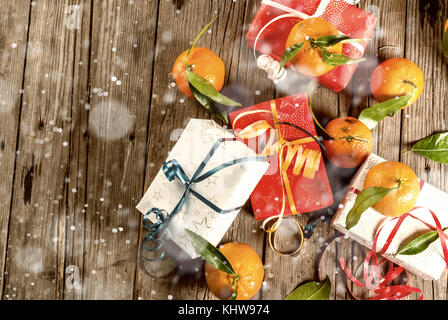 Natale e Anno Nuovo concetto di mandarini freschi con foglie verdi in un cestello di bianco, decorazione di Natale e confezioni regalo, sulla vecchia tavola in legno rustico, Foto Stock