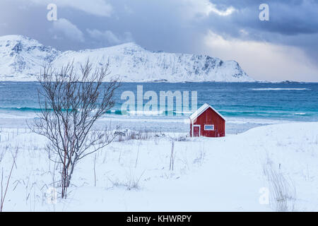Una tipica casa di pescatori chiamato rorbu sulla spiaggia innevata incornicia il mare ghiacciato a Ramberg Isole Lofoten in Norvegia Europa Foto Stock