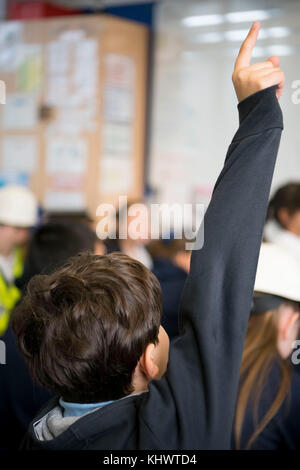 Un giovane bambino bianco mette la mano fino quando ha chiesto una domanda in un aula scolastica in Galles, nel Regno Unito. Foto Stock