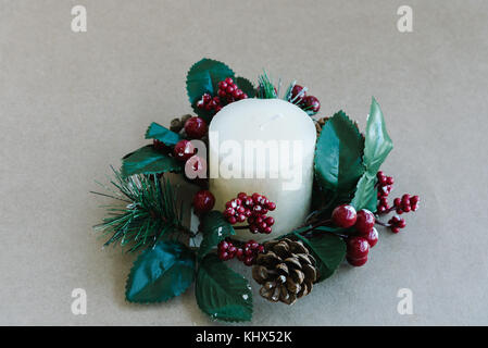 Vacanze di Natale ornamenti con candela bianca e foglie di santo con bacche di colore rosso su sfondo rustico Foto Stock