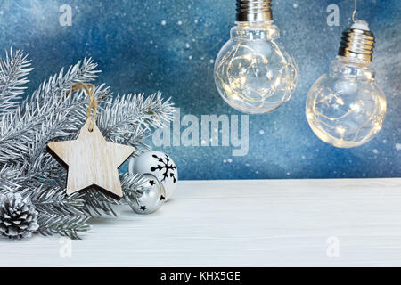 Argento di abete di Natale ramo di albero, albero decorazioni e incandescente retrò lampadine su sfondo blu Foto Stock