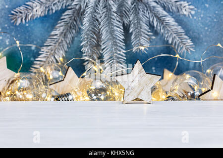 Argento abete natalizio il ramo di un albero in legno rustico stelle e incandescente vecchio garland lampade su sfondo blu Foto Stock