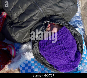 Donna con tappo blu sopra gli occhi si crogiola in una giornata di vento presso la spiaggia del Mare del Nord. Foto Stock