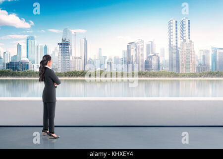 Ritratto di asian business woman standing sulla terrazza e guardare paesaggio urbano moderno a luce del giorno Foto Stock