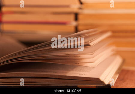 Libro aperto contro lo sfondo di una pila di altri libri, in tinta calda Foto Stock