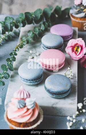 Macarons pastello, tortine e fiori su sfondo marmo. I dolci di nozze, nozze tortine e amaretti. Messa a fuoco selettiva Foto Stock