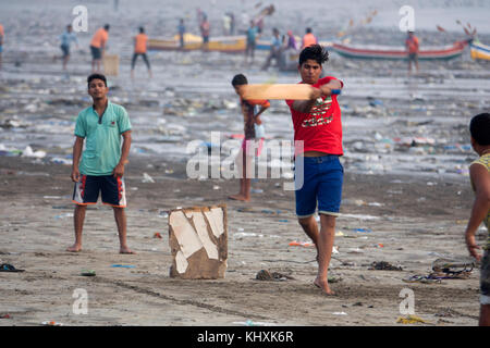 Indian ragazzi adolescenti gioco di cricket tra immondizia di plastica e altri rifiuti su versova beach, Mumbai Foto Stock