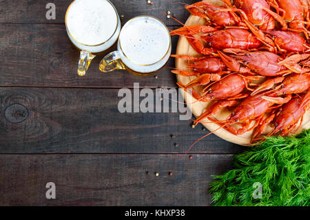 Un mucchio di gustosi aragosta bollita su un round vassoio in legno e due boccali di birra fredda su uno sfondo scuro. vista dall'alto. spazio libero per un'iscrizione. Foto Stock