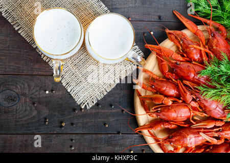 Un mucchio di gustosi aragosta bollita su un round vassoio in legno e due boccali di birra fredda su uno sfondo scuro. vista dall'alto. spazio libero per un'iscrizione. Foto Stock