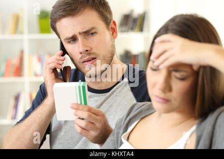 Il marito aiutando la sua moglie malata medico di chiamata sul telefono seduto su un divano a casa Foto Stock