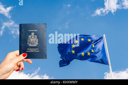 Unione europea (UE) bandiera contro un cielo blu con digital composito della donna in possesso di un passaporto canadese Foto Stock