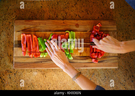 Vista aerea della donna e delle sue mani trinciatura di peperoni rossi e verdi Foto Stock