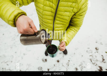 Elevato angolo collo in giù in vista di un escursionista maschio versando il caffè da pallone nella neve Foto Stock