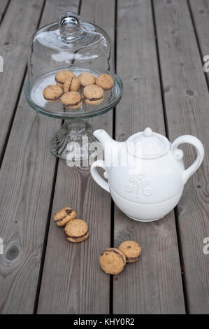 Lady's baci - italiana di nocciole cookies sandwich sulla torta con piedistallo bianco teiera ceramica Foto Stock