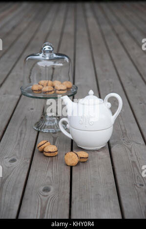 Lady's baci - italiana di nocciole cookies sandwich sulla torta con piedistallo bianco teiera ceramica Foto Stock