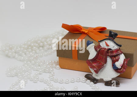 Confezione regalo con un fiocco di colore arancione, bianco perline, toy pupazzo di neve Foto Stock