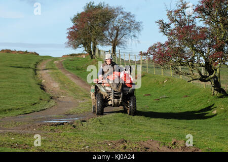 Contadino in Galles in sella a un quad con il suo cane da pecora sotto il sole invernale Powys Wales UK Foto Stock