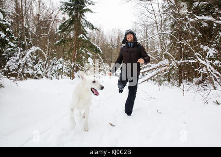 Giovane uomo che corrono nella foresta con Pastore Svizzero bianco cane Foto Stock