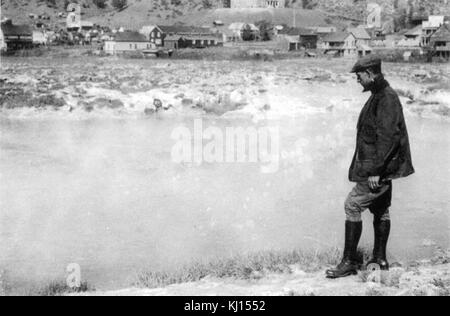 Questa fotografia vintage cattura un uomo in piedi vicino a un fiume. L'immagine riflette la vita dei primi anni del XX secolo, mostrando la connessione tra gli individui e la natura. Foto Stock