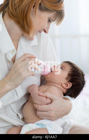 Madre dando baby acqua dalla bottiglia seduta sul letto Foto Stock