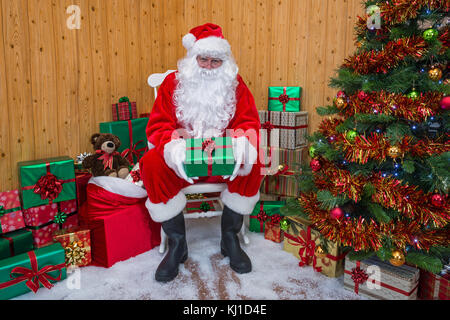 Babbo Natale nella sua grotta circondata da un albero di Natale con regali e dono scatole confezionate Foto Stock