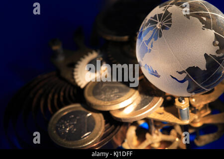 Globo di vetro giacente su ingranaggi e monete su sfondo blu scuro Foto Stock