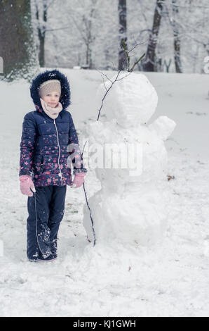 Bambino felice ennjoying atmosfera invernale in parcheggio coperto da neve giocando e costruire un pupazzo di neve Foto Stock