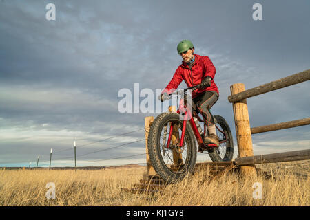 Un senior maschio è in sella ad una mountain bike di grasso su una guardia del bestiame in pietra ollare Prairie Area naturale nel nord del Colorado, tardo autunno scenario Foto Stock