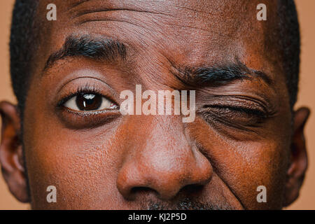 Il squint di afro american elegante uomo al marrone parete studio Foto Stock