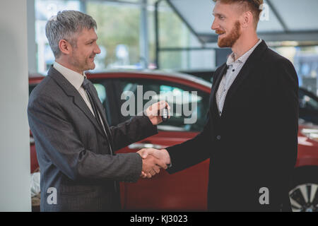 Auto il venditore ed il compratore si stringono la mano in auto showroom. Foto Stock