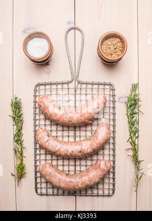 Salame crudo per friggere grigliate di menzogna sulla griglia per la cottura con rosmarino e spezie su di un legno bianco sfondo rustico, vista dall'alto Foto Stock