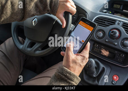 Irresponsabile uomo al volante l'invio di un messaggio mediante la messaggistica di testo / texting su smart phone / smartphone / cellulare mentre si guida auto sulla strada Foto Stock
