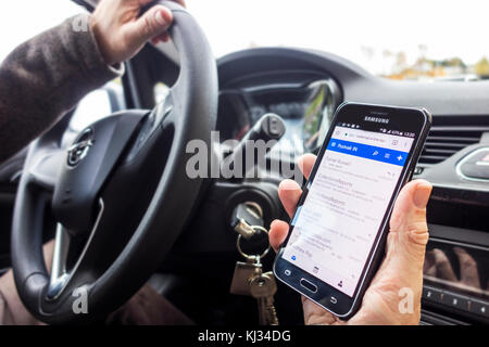 Irresponsabile uomo al volante dei messaggi di controllo sulla smart phone / smartphone / cellulare mentre si guida auto sulla strada Foto Stock