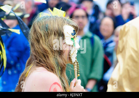 Interprete femminile che indossa una maschera di porcellana nel carnevale del edinburgh jazz e blues festival che si muove in basso lungo il tumulo verso Princes street Foto Stock