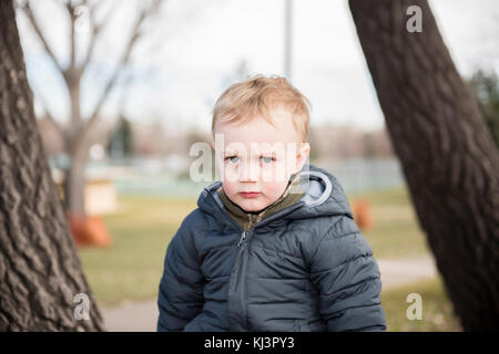 Ritratto di un bimbo piccolo ragazzo al di fuori di un parco locale. Vestito calorosamente per l'inverno. Foto Stock