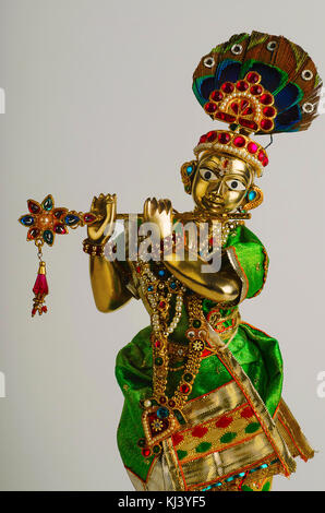 Statua in ottone di Lord Krishna con flauto (vista parziale) con mukut o corona su sfondo grigio chiaro Foto Stock