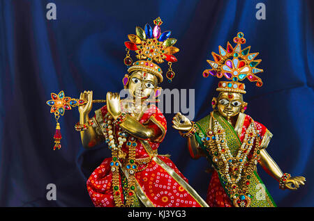 Statua in ottone di Lord Krishna con flauto e Radha (vista parziale) con mukut o corona su sfondo blu scuro Foto Stock